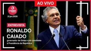 Uma imagem promocional de "Poder Entrevista" para uma entrevista ao vivo com Ronaldo Caiado. Caiado, governador de Goiás e pré-candidato à Presidência da República, está de pé em um púlpito com microfones, com o punho esquerdo fechado em um gesto de ênfase. Ele veste terno azul-escuro, camisa branca e gravata azul-clara estampada. O fundo escuro mostra uma bandeira do Brasil desfocada. O texto na imagem inclui: "PODER ENTREVISTA", "21.jan.2026", "AO VIVO", "ENTREVISTA", "RONALDO CAIADO" e "governador de Goiás e pré-candidato à Presidência da República".