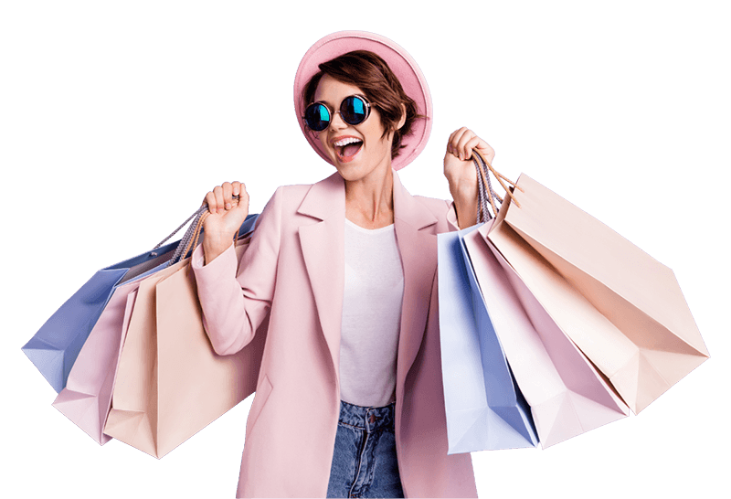 Mulher vestida com blazer e chapeu rosa, calça jeans e camiseta branca, com sacolas erguidas nas duas mãos, comprando de negócios locais